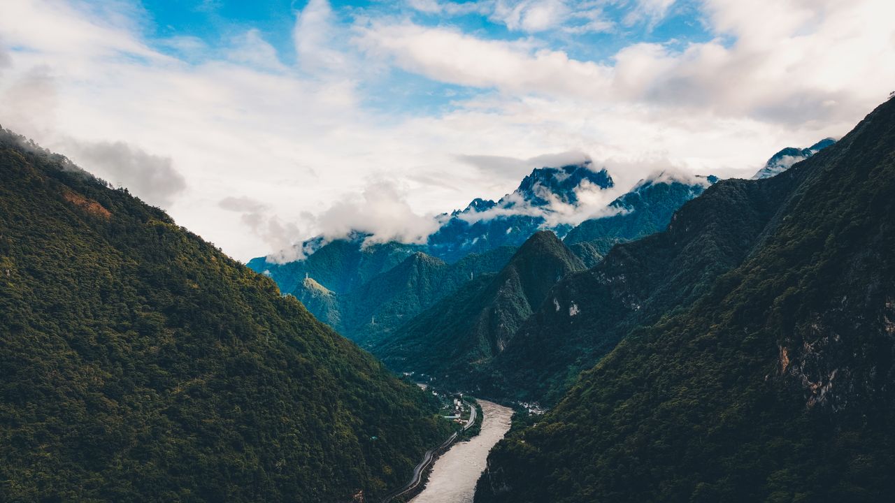 Stunning aerial view of Nujiang Valley in Yunnan, China, showcasing lush green mountains and a winding river under a dramatic sky.